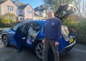 A man standing next to a blue car filled to the brim with blankets for Ukraine appeal
