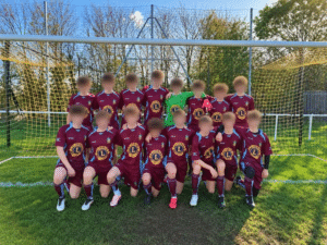 A youth football team posing in front of a football goal wearing their new kit for a team photo